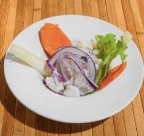 Plato de ceviche fresco con cebolla morada, lechuga, zanahoria y trozos de pescado blanco, servido en un plato blanco sobre una mesa de madera.