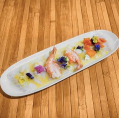 Plato de ceviche de camarones decorado con flores comestibles y servido sobre una base de madera. Ideal para amantes de la gastronomía gourmet.